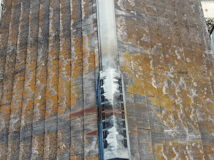 棟板金が錆び、苔やカビが生えて全体的に劣化が進んでいる状態のスレート屋根