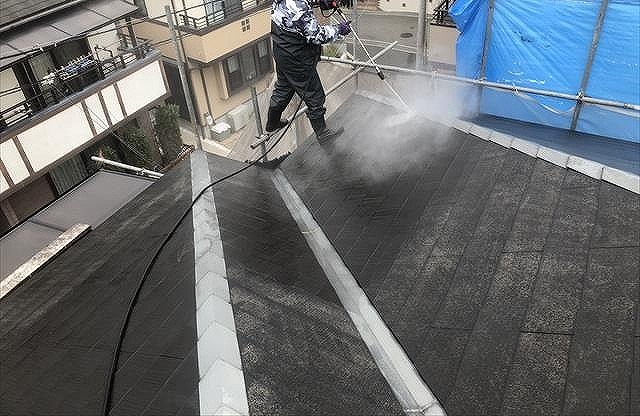 高い屋根の上で高圧洗浄を行う職人