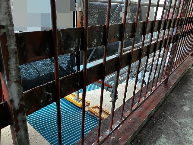 甲府市で屋上の鉄部手すり・鉄部柵に、電動工具(サンダー)でケレン作業(研磨・目粗し)する様子