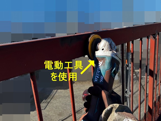 甲府市で屋上の鉄部手すり・鉄部柵に、電動工具(サンダー)でケレン作業(研磨・目粗し)する様子