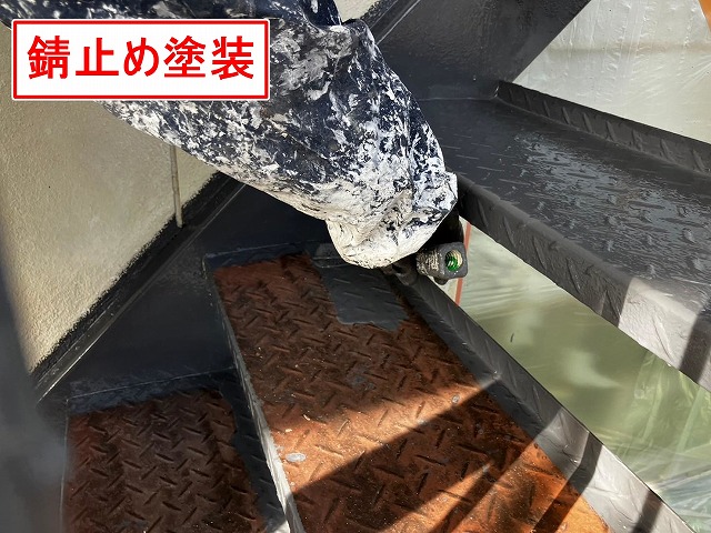 甲府市で塗膜剝がれ・錆びの発生した鉄部階段にケレン作業後、錆止め塗装(下塗り)を行う様子